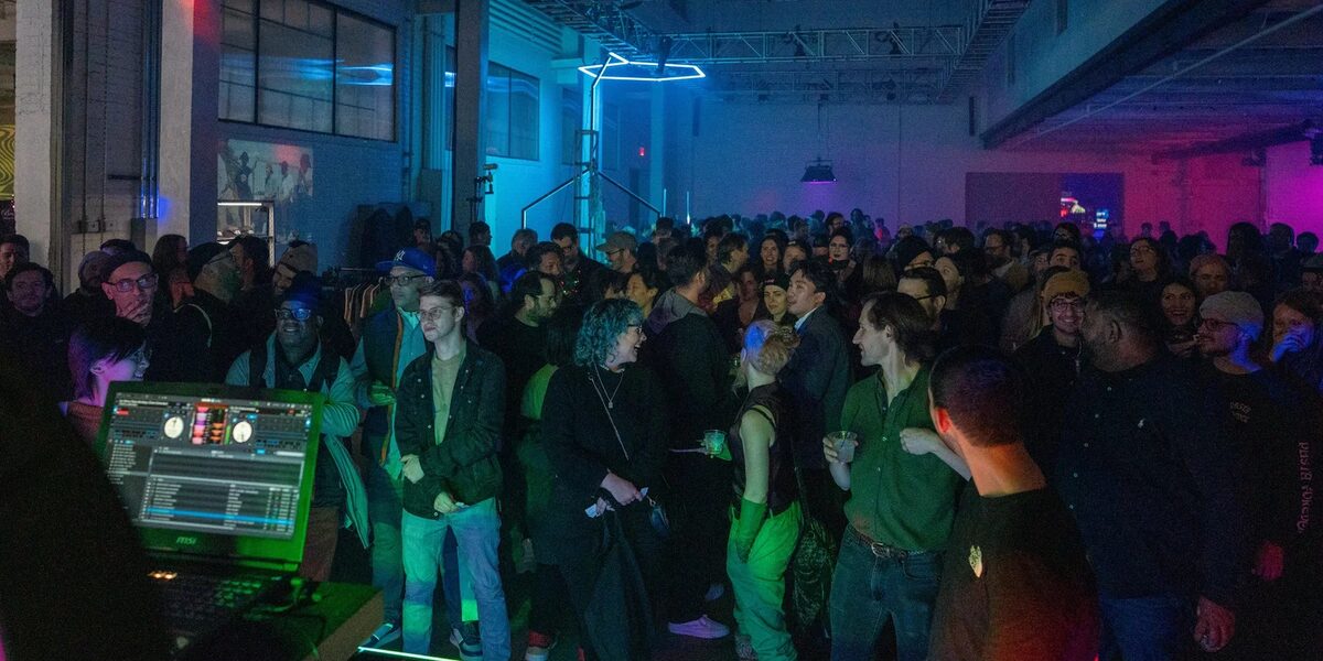 A crowded Salon holiday party in a warehouse, lit blue and magenta